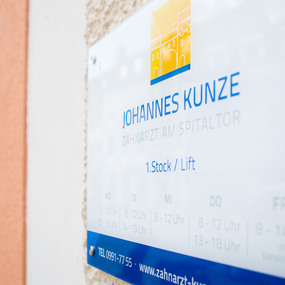 Praxisschild einer Zahnarztpraxis mit Öffnungszeiten und barrierefreiem Zugang.