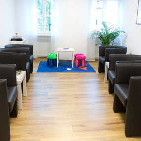 Modernes Wartezimmer mit schwarzen Sesseln, Kinderspielecke, Zeitschriften und Pflanzen.