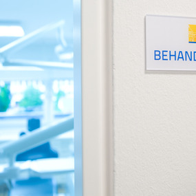 Eingang zu einem modernen Behandlungsraum in einer Zahnarztpraxis mit Schild.